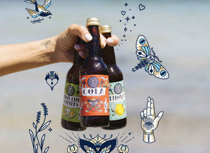 Hand holding Waves & Caves bottles with beach and illustrations in the background