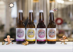 Row of rok Kombucha bottles with decorative figures on a white surface.